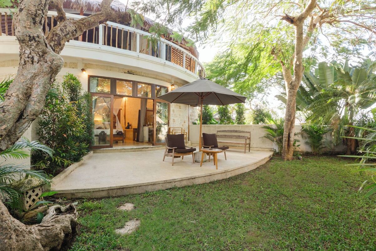 Ein Haus mit einem geschwungenen Balkon, Sitzgelegenheiten im Freien und üppiger Bepflanzung.