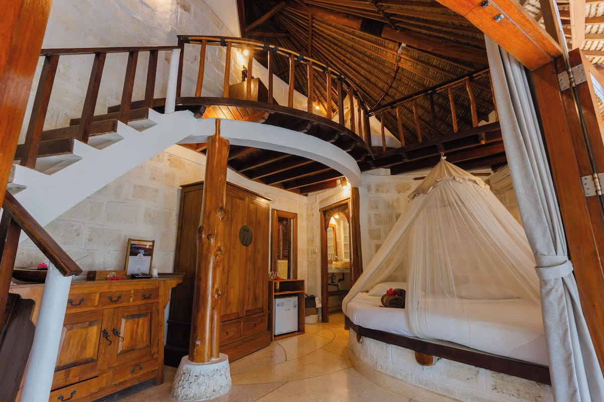 Ein Schlafzimmer mit einer Wendeltreppe, Holzmöbeln, einem Himmelbett und einer Steinwand.