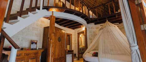 A bedroom with a curved staircase, wooden furniture, a canopy bed, and a stone wall.
