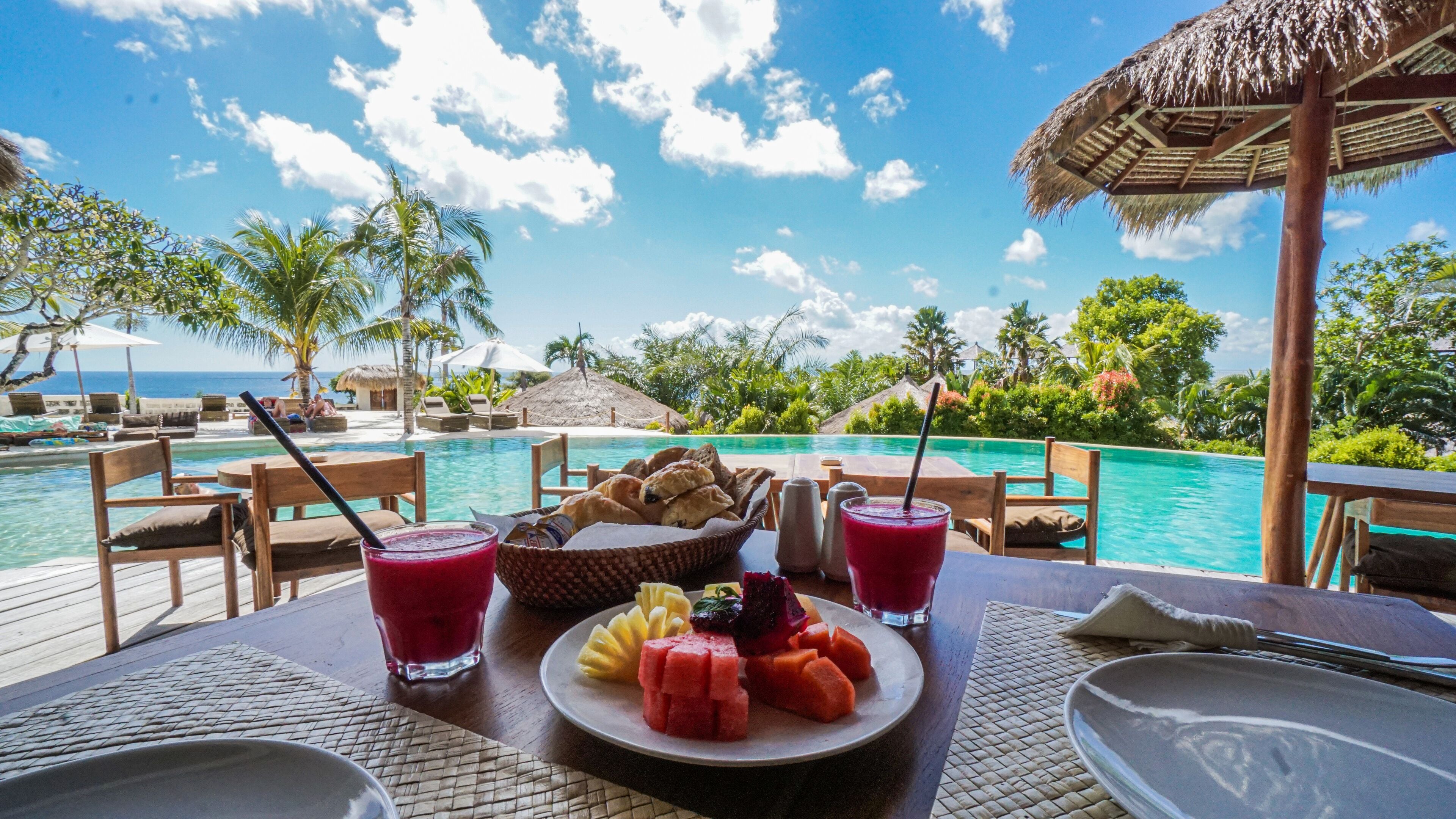 A poolside dining area with a table set for a meal, overlooking a pool and ocean view.