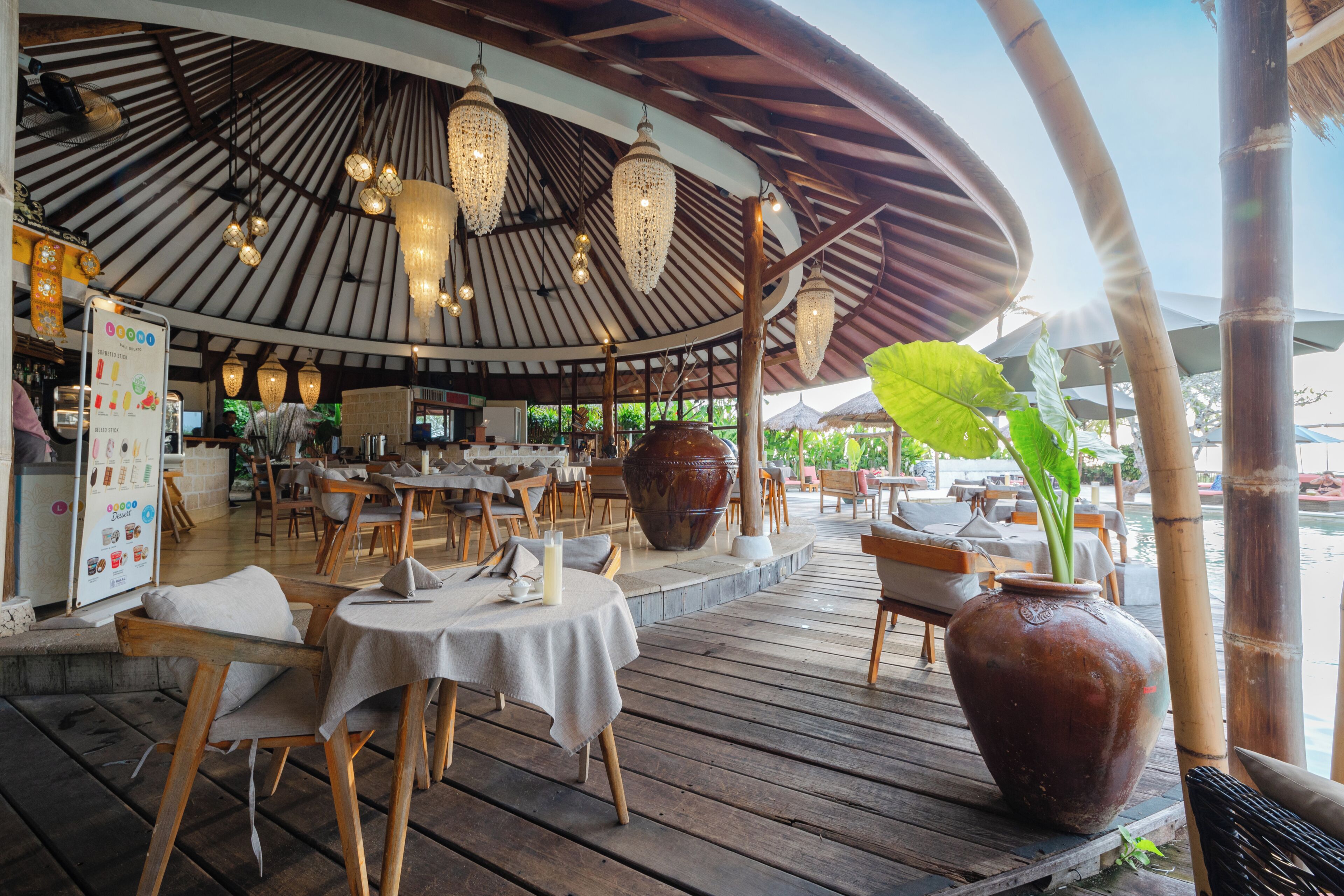 Een terrasrestaurant met houten tafels, hangende lampen en een grote vaas.