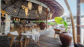 Een terrasrestaurant met houten tafels, hangende lampen en een grote vaas.