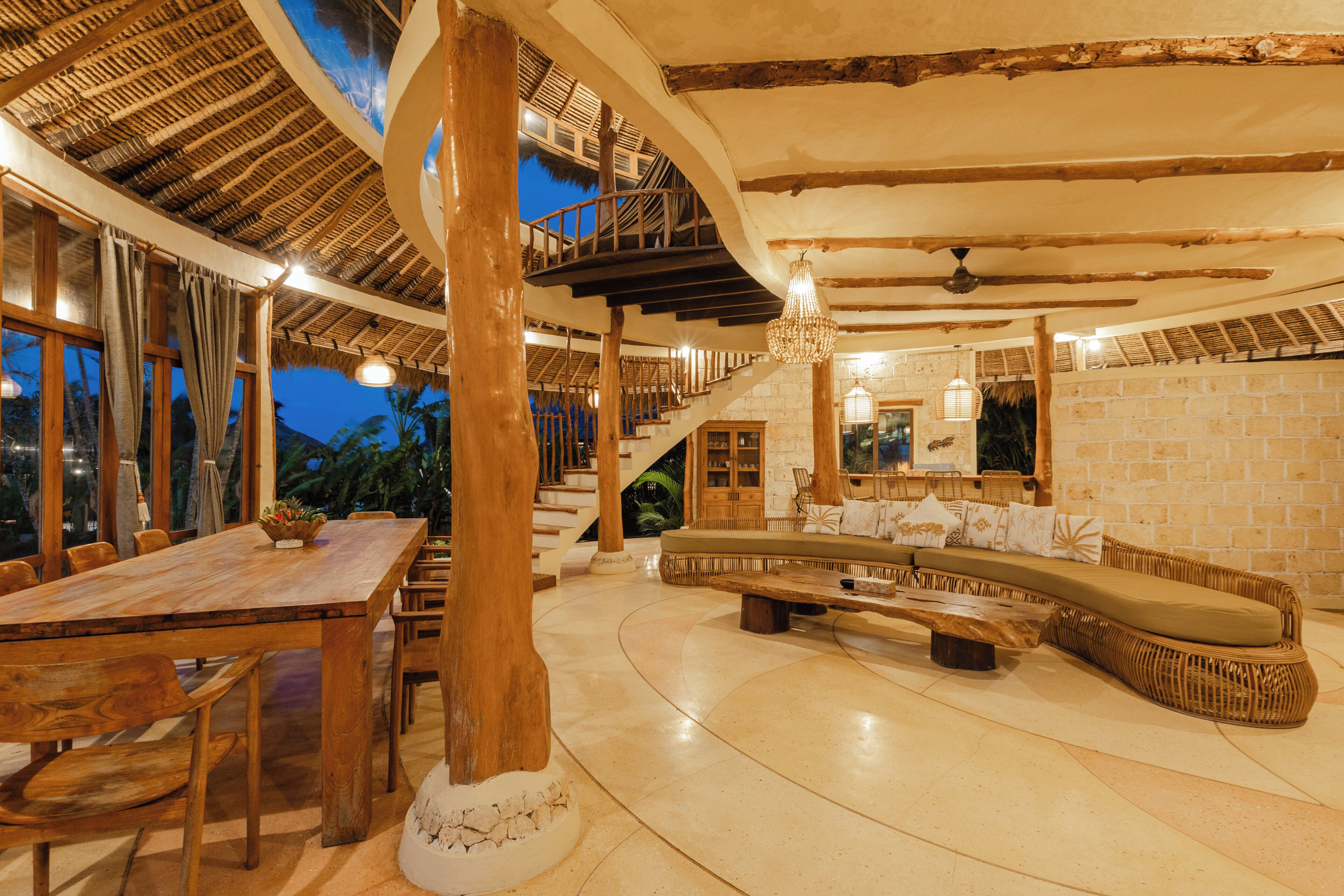 A spacious interior with a wooden dining table, a curved seating area, and a staircase leading to an upper level.