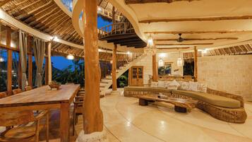 A spacious interior with a wooden dining table, a curved seating area, and a staircase leading to an upper level.