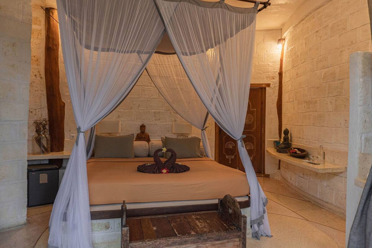 Ein Zimmer mit einem Bett, einer Statue, einem kleinen Tisch und einer Bank.