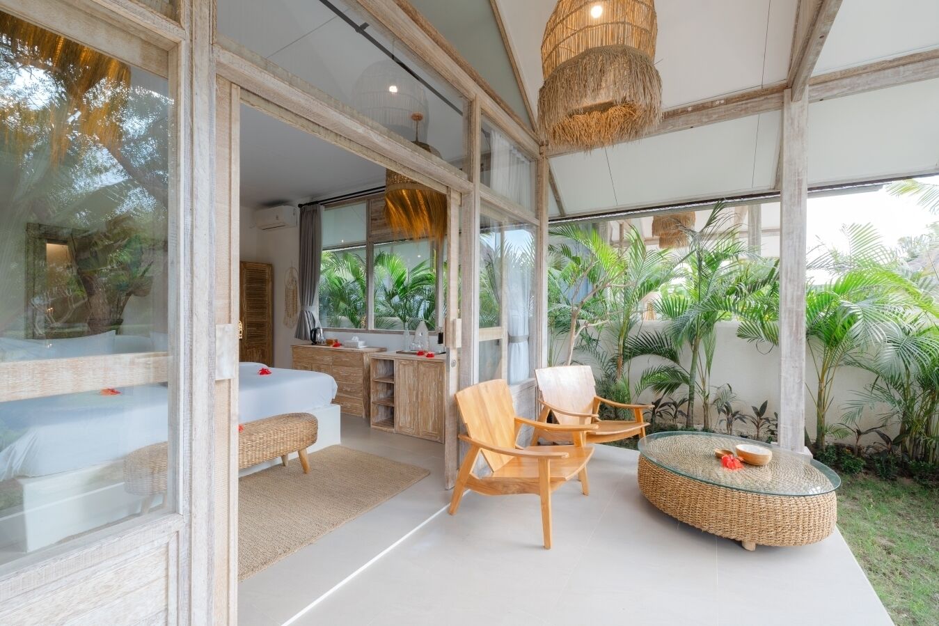 Een moderne kamer met een grote glazen deur die uitkomt op een balkon, houten meubels en een geweven salontafel.
