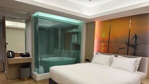 A modern hotel room with a large bed, a glass-enclosed shower, a desk with a coffee maker, and a sunset mural on the wall. - Viva Hotel Songkhla (Songkhla)