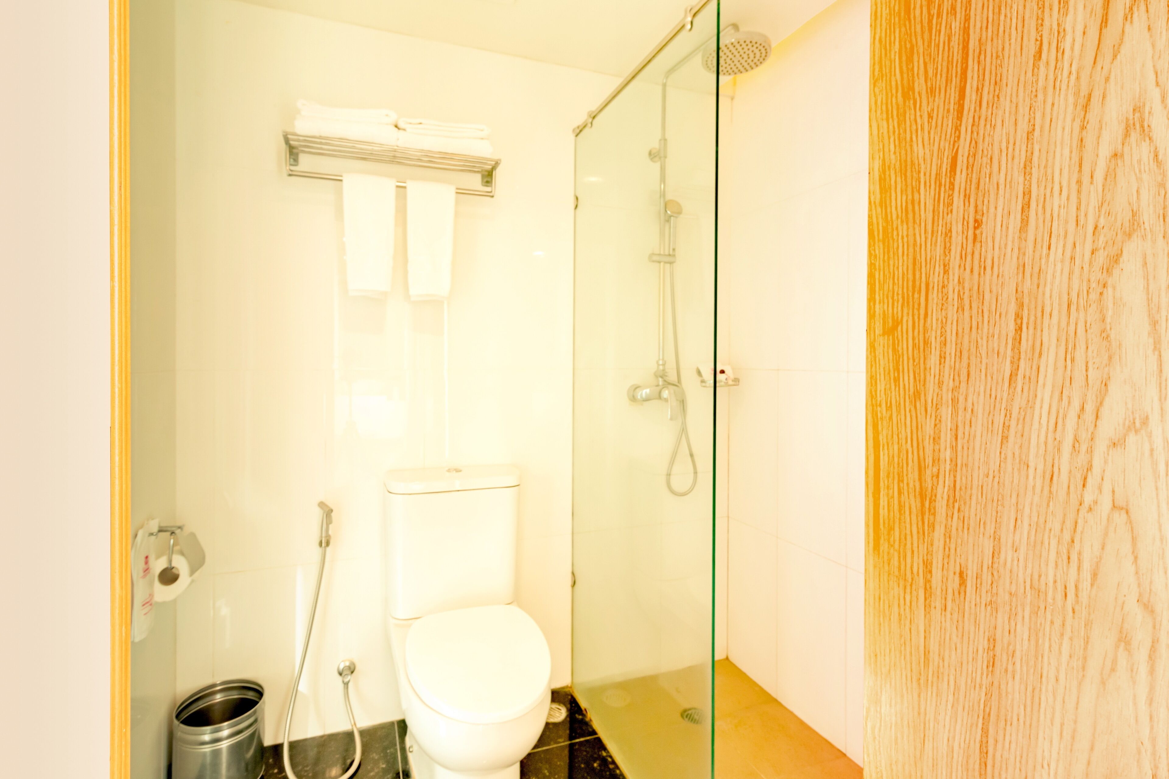 A bathroom with a toilet, a glass shower enclosure, and a metal trash can.