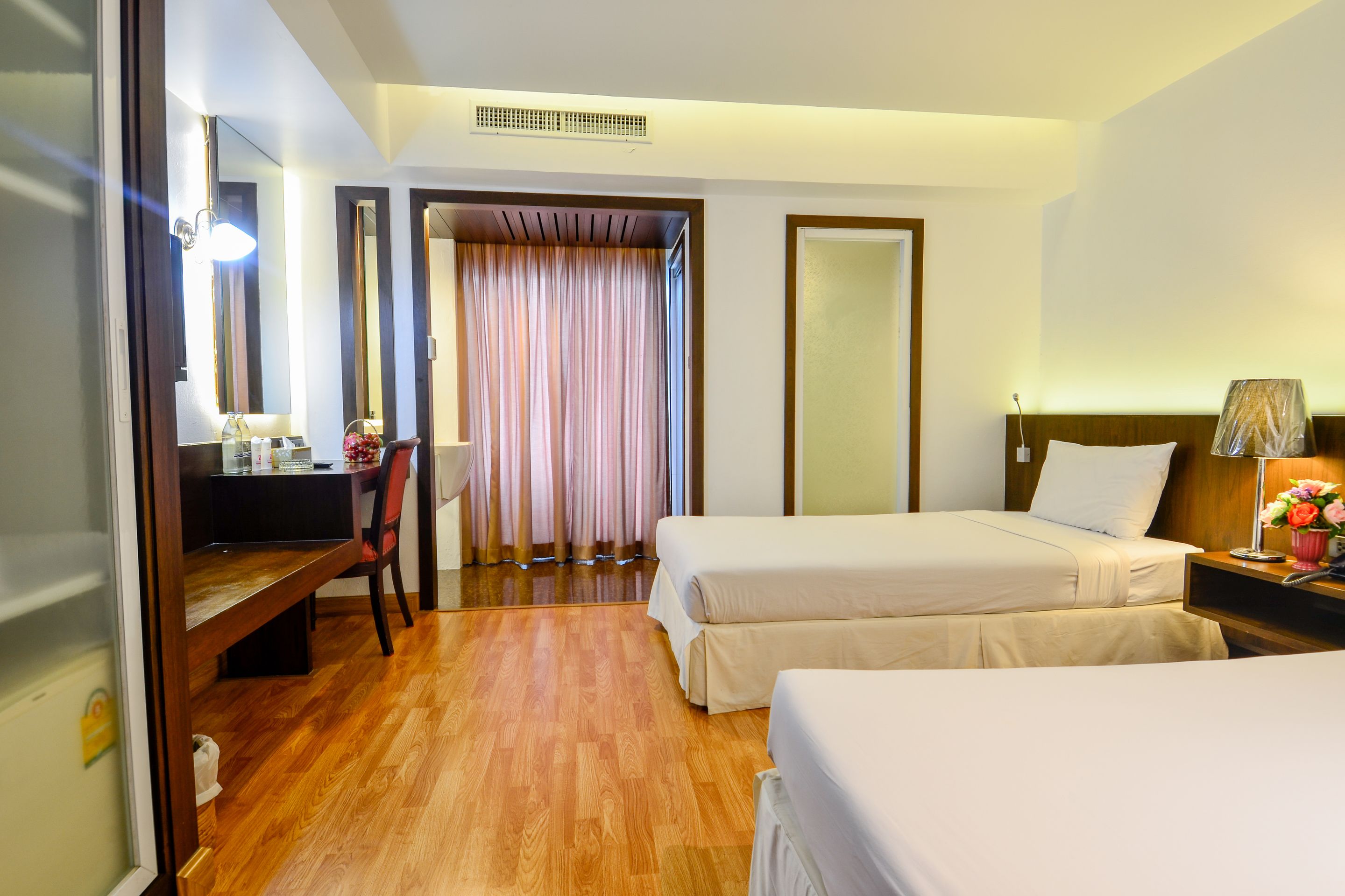 Une chambre d’hôtel avec deux lits, un bureau avec une chaise, un miroir et une fenêtre avec des rideaux.
