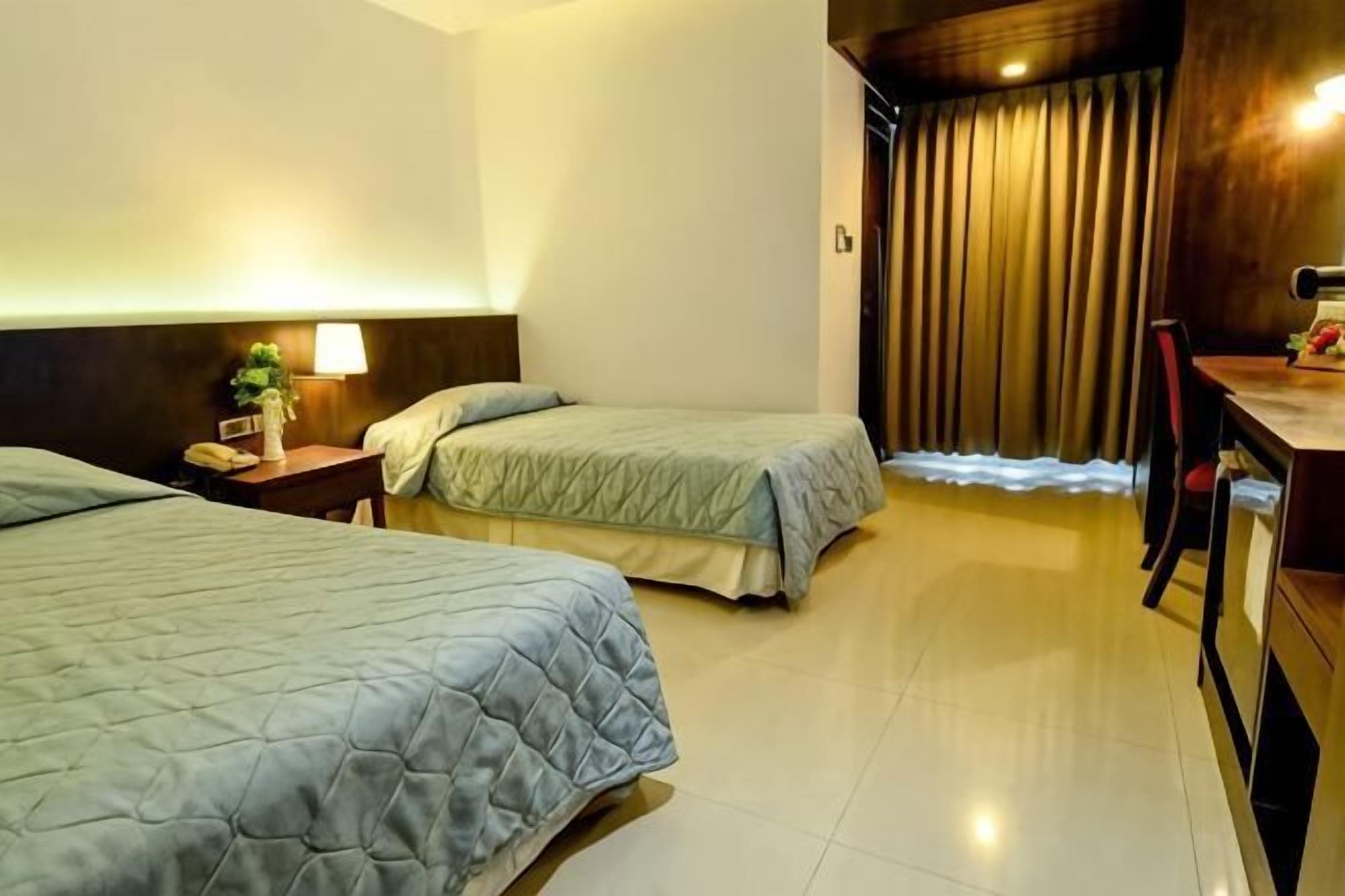 Une chambre d’hôtel avec deux lits, un bureau, une chaise, une table de chevet et un rideau.