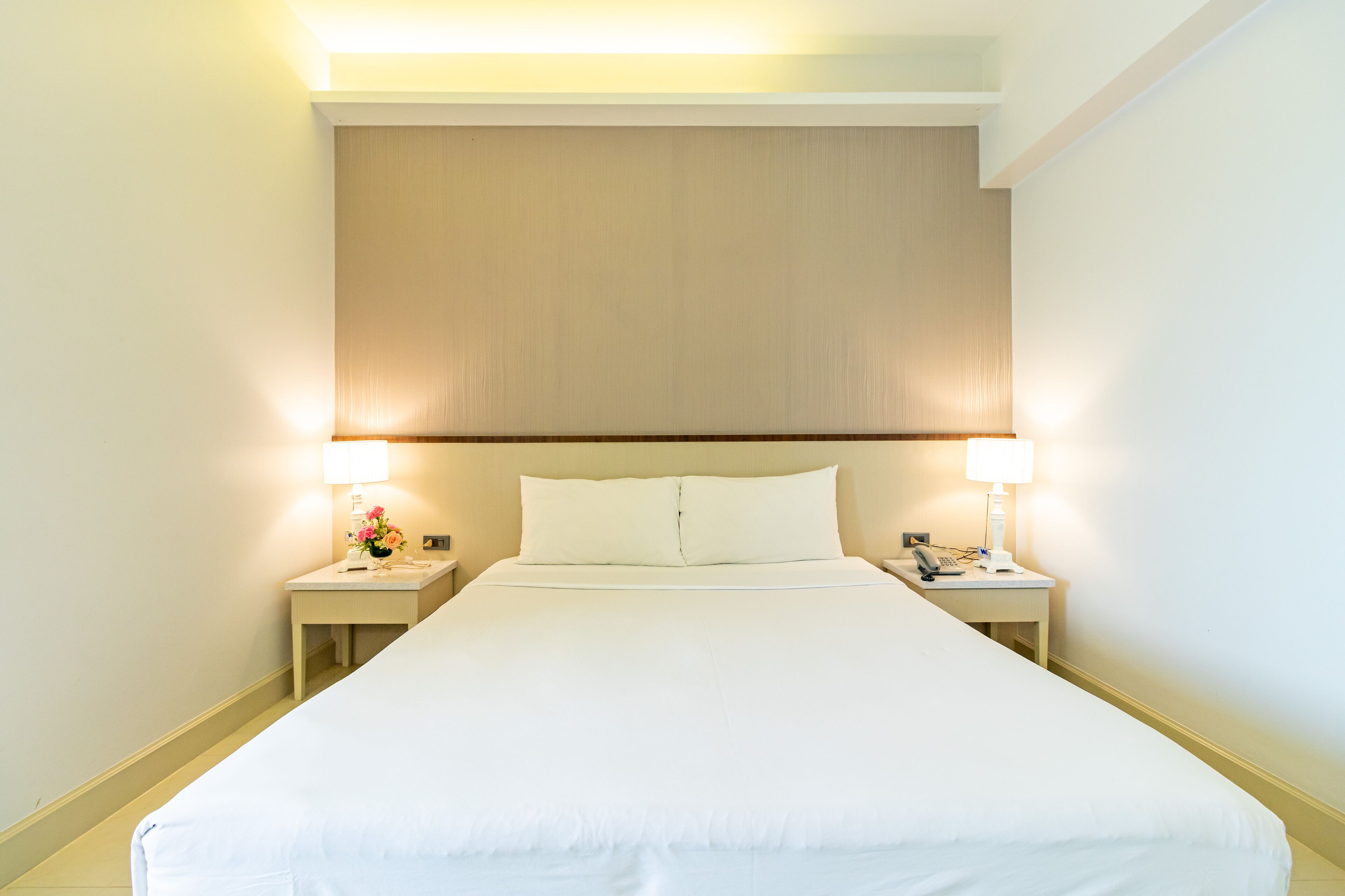 Una habitación de hotel con una cama grande, dos mesitas de noche con lámparas y una decoración en tonos neutros.