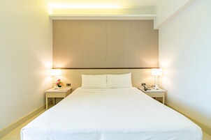 Una habitación de hotel con una cama grande, dos mesitas de noche con lámparas y una decoración en tonos neutros.