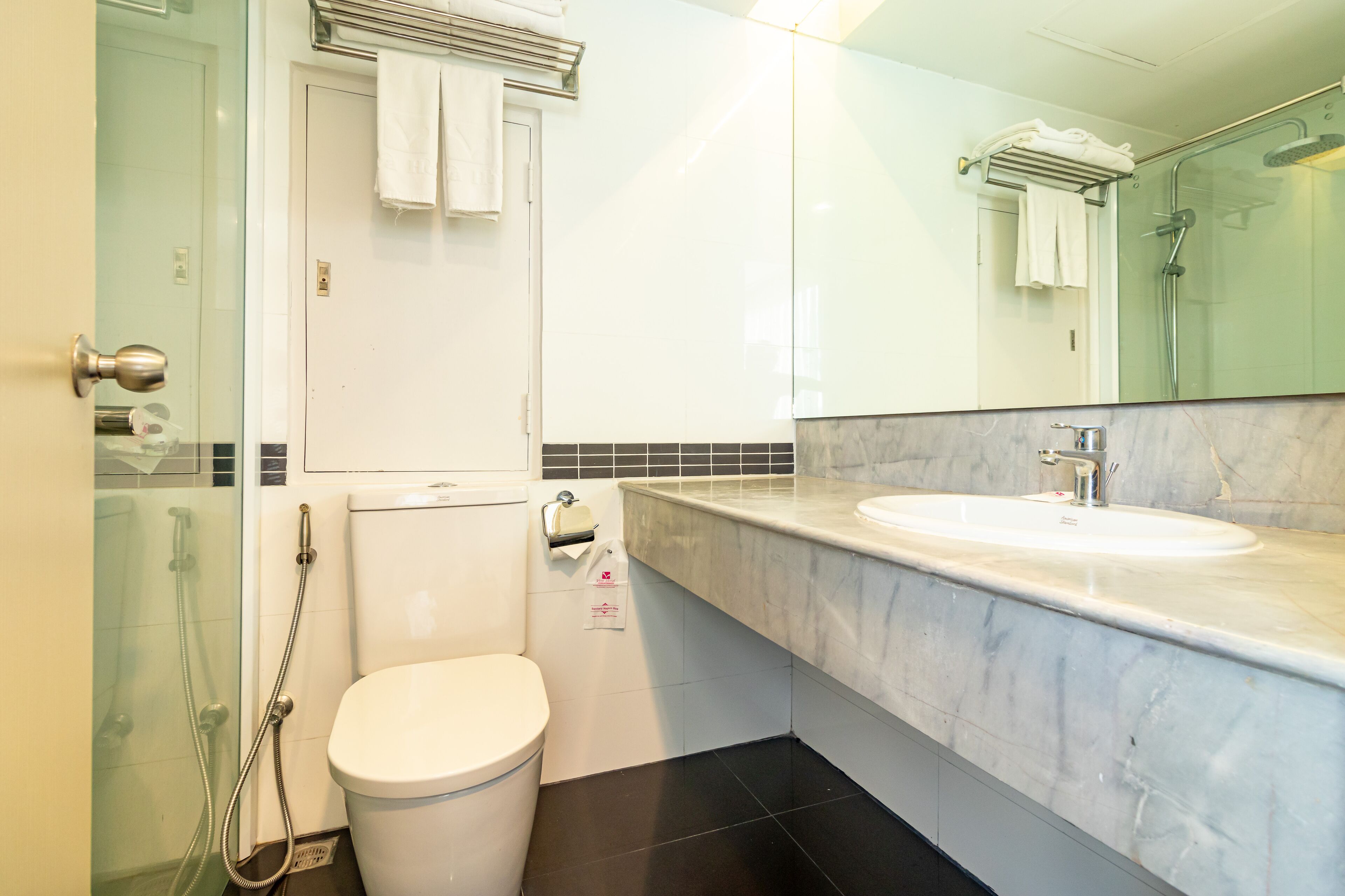 A modern bathroom with a glass shower enclosure, a white toilet, a marble sink, and a large mirror.