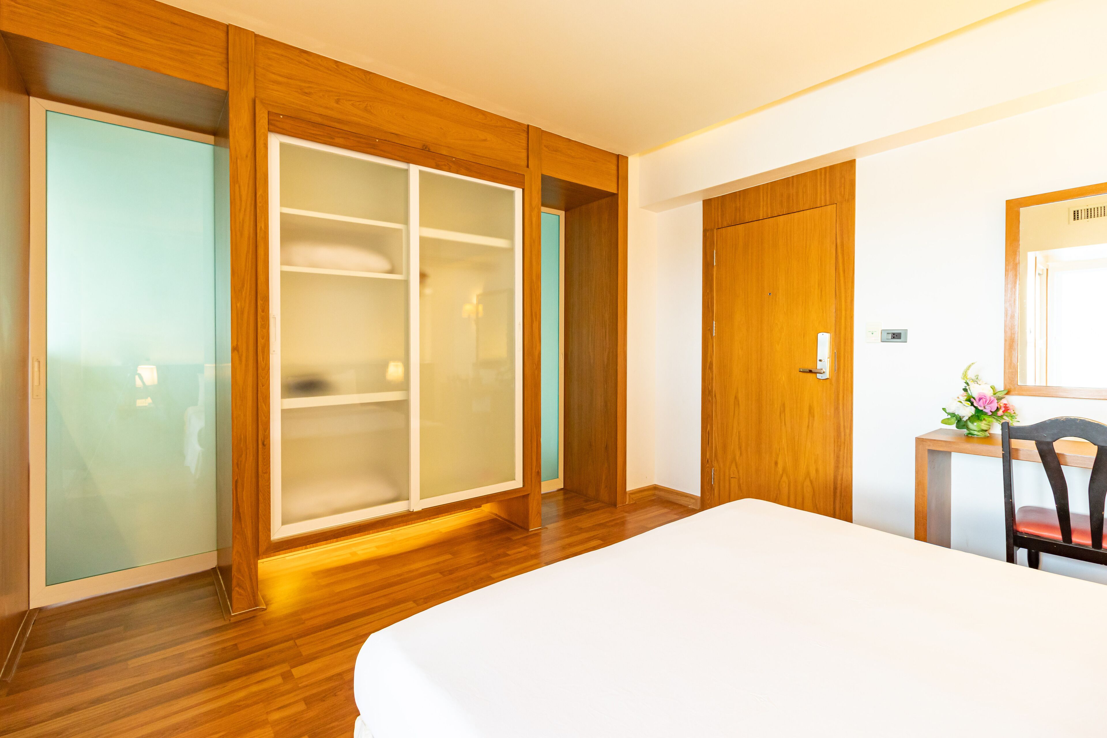 A bedroom with a wooden floor, a bed, a wardrobe, and a desk with a chair.