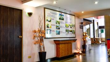 Een hotel receptie met een groot informatief poster, een houten receptiebalie en potplanten.