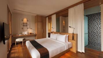 A modern hotel room with a large bed, wooden flooring, a desk with a chair, a TV, and a bathroom with a tiled shower.
