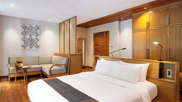A hotel room with a large bed, a sofa, a small table with a fruit bowl, and wooden cabinets.