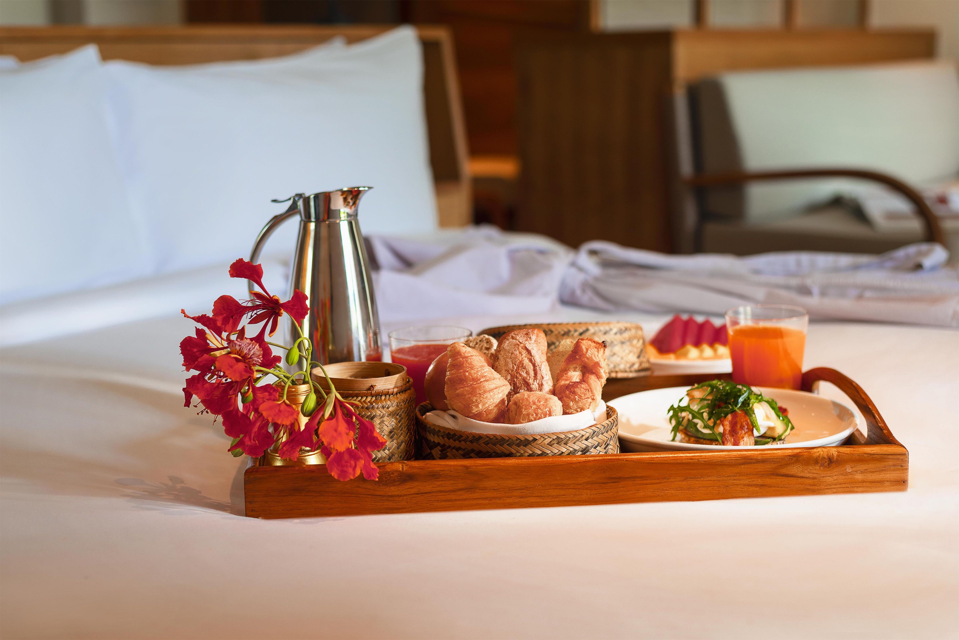 Ein Frühstücksbrett mit Brot, einer Karaffe und einem Glas Orangensaft auf einem Bett.