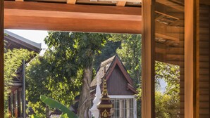 Un balcon en bois avec une table dressée pour le petit-déjeuner, offrant une vue sur un bâtiment traditionnel et une végétation luxuriante.