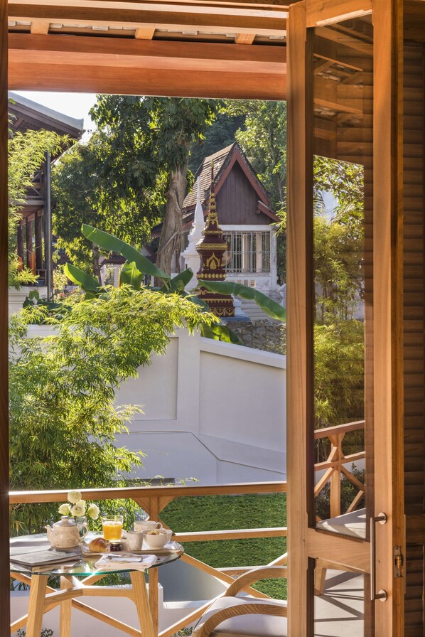 Un balcon en bois avec une table dressée pour le petit-déjeuner, offrant une vue sur un bâtiment traditionnel et une végétation luxuriante.