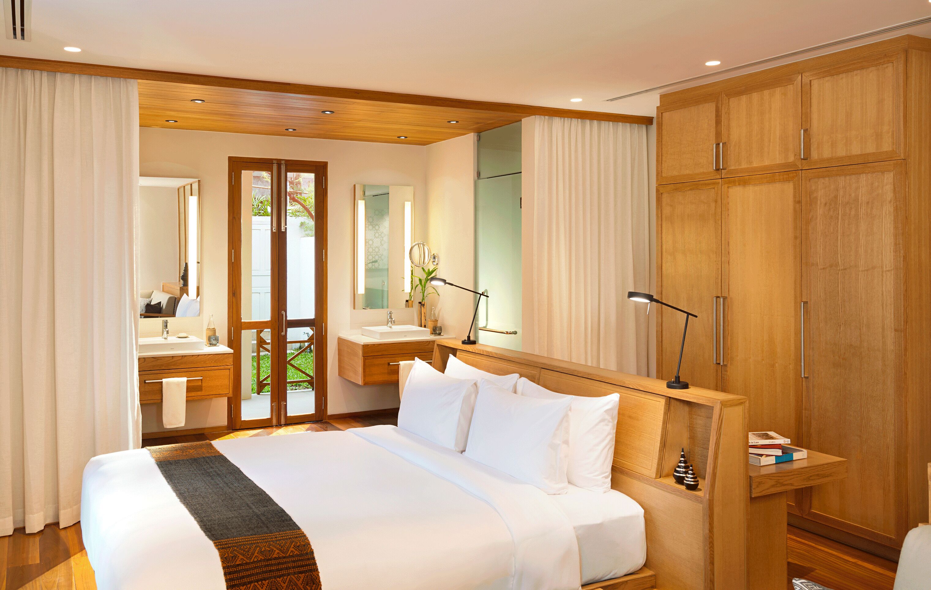 Ein modernes Hotelzimmer mit einem großen Bett, einem Holzschrank und einem Badezimmer mit Waschtisch und Spiegel.
