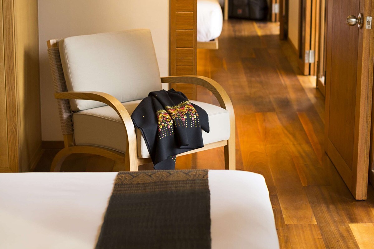 A hotel room with a bed, a chair, a wooden floor, and a wardrobe.