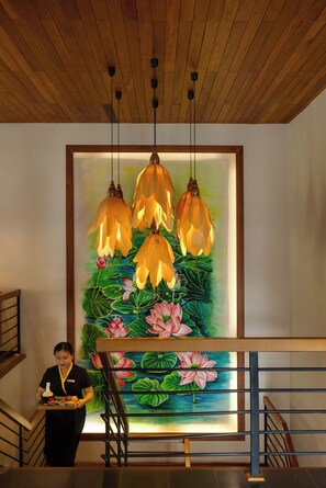 Un escalier avec une rampe, un mur orné d’une peinture florale et un plafond avec des poutres en bois et des luminaires suspendus.