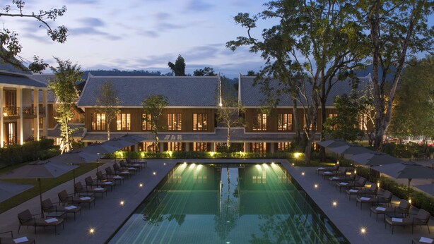 Un hôtel doté d’une grande piscine extérieure, d’un espace détente avec des fauteuils et d’un bâtiment traditionnel avec un toit en tuiles.