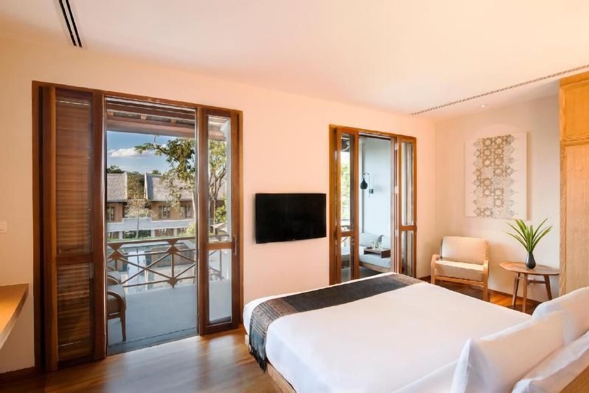 A hotel room with a bed, a TV, a chair, a small table, and a balcony with a view.