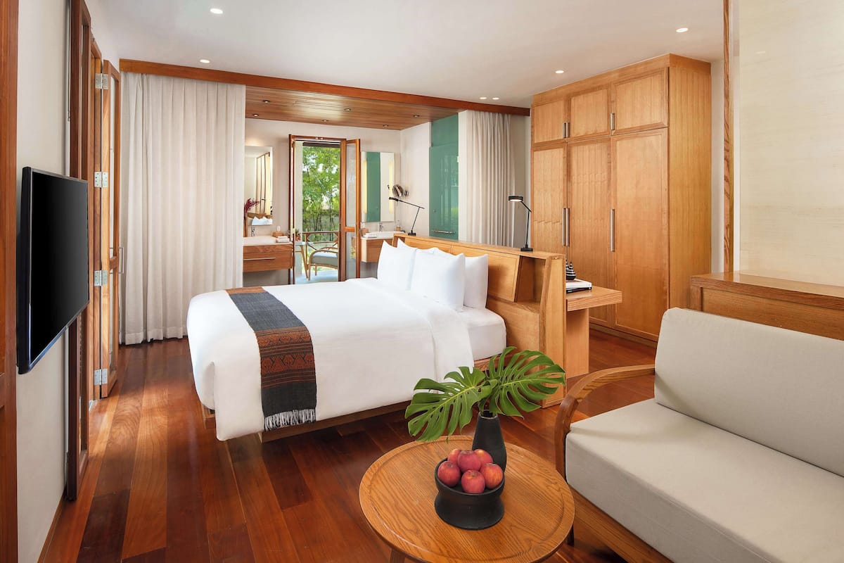 Une chambre d’hôtel avec un lit, un canapé, une télévision, une plante et une petite table.