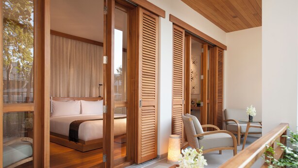 Een moderne slaapkamer met een groot bed, houten luiken en een zithoek met een tafel en stoelen.