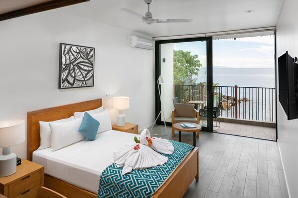 A hotel room with a bed, bedside table, lamp, artwork, and a balcony with a view of the sea. - Coral Sea Resort & Casino (Honiara)