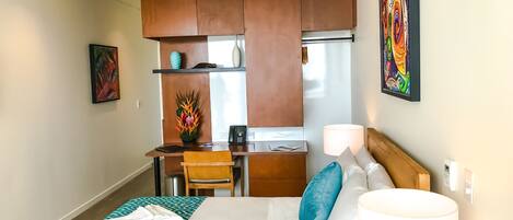 Habitación de hotel con cama, escritorio, silla, kitchenette pequeña y ventilador de techo.