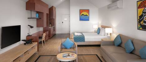 Una habitación de hotel moderna con televisor de pantalla plana, un sofá, una cama con almohadas azules, una mesita de centro y un cuadro en la pared.