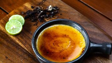 Un bol de soupe avec une anse noire, accompagné de tranches de citron vert et de quelques épices, le tout présenté sur une planche en bois.