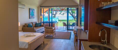 A modern hotel room with a bed, a sofa, a dining area, and a view of the beach.