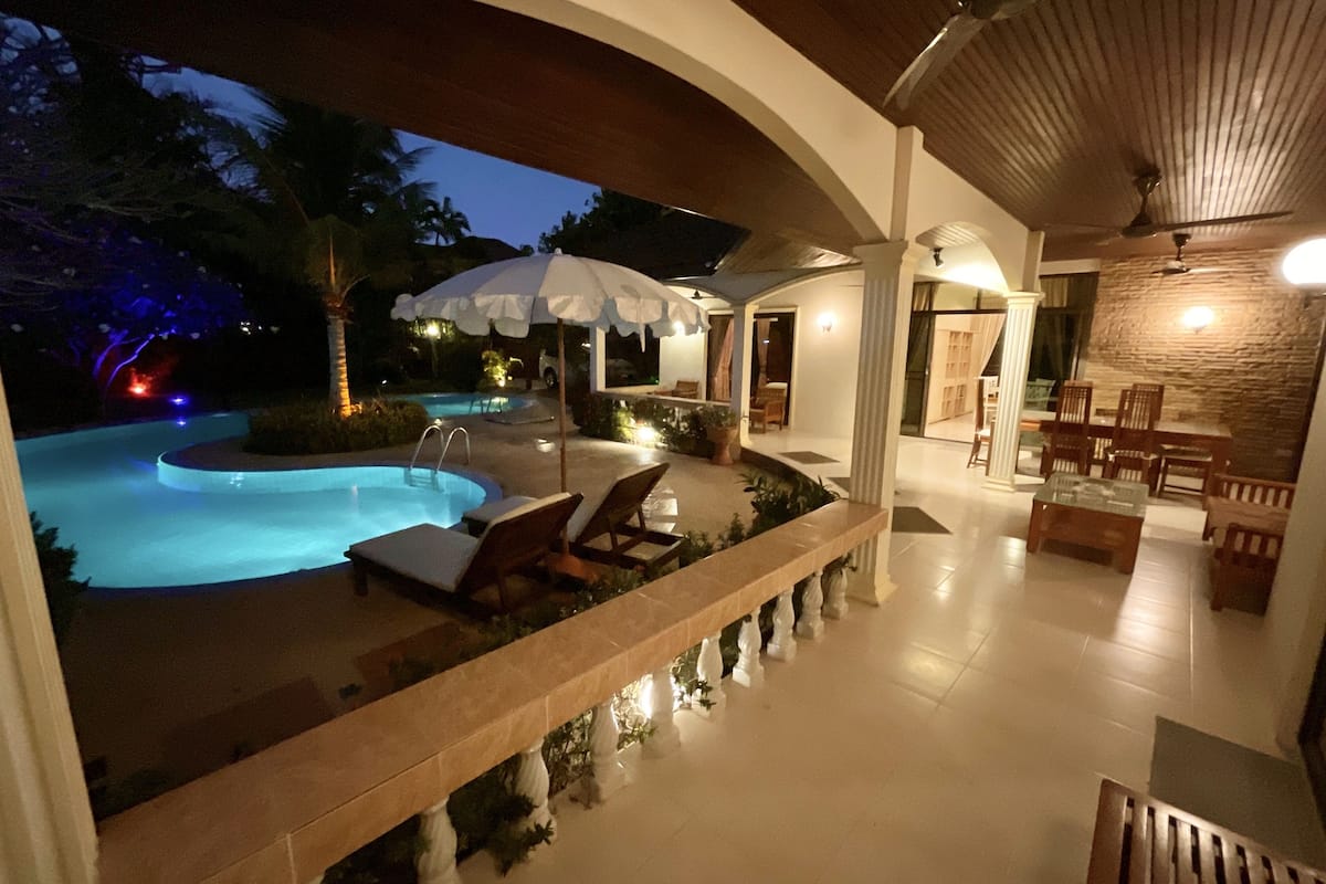 A poolside area with lounge chairs, a covered seating area, and a stone wall.