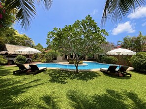 A swimming pool surrounded by grass, with lounge chairs and umbrellas. - Coconut Paradise Holiday Villas (Rawai)