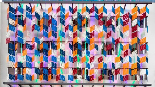 Un bâtiment moderne à la façade colorée, ornée de motifs géométriques, et doté d’une grande entrée avec des marches.