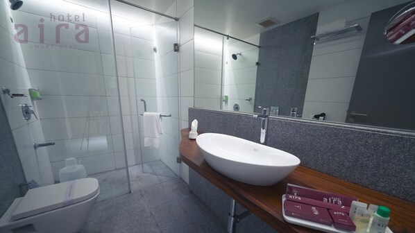 A modern bathroom with a glass-enclosed shower, a large white sink, and a vanity with toiletries.