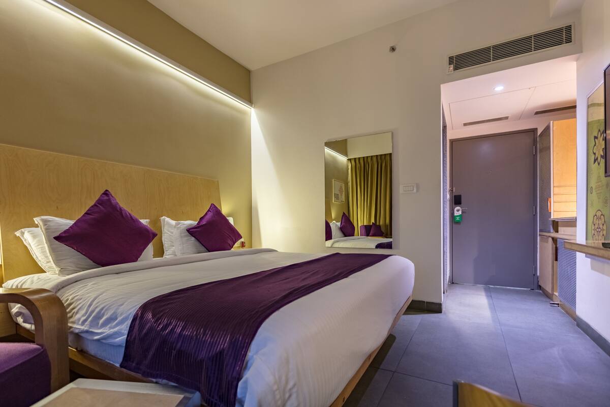 Ein Hotelzimmer mit einem Bett, einem Nachttisch, einem Spiegel und einer Tür zu einem anderen Raum.