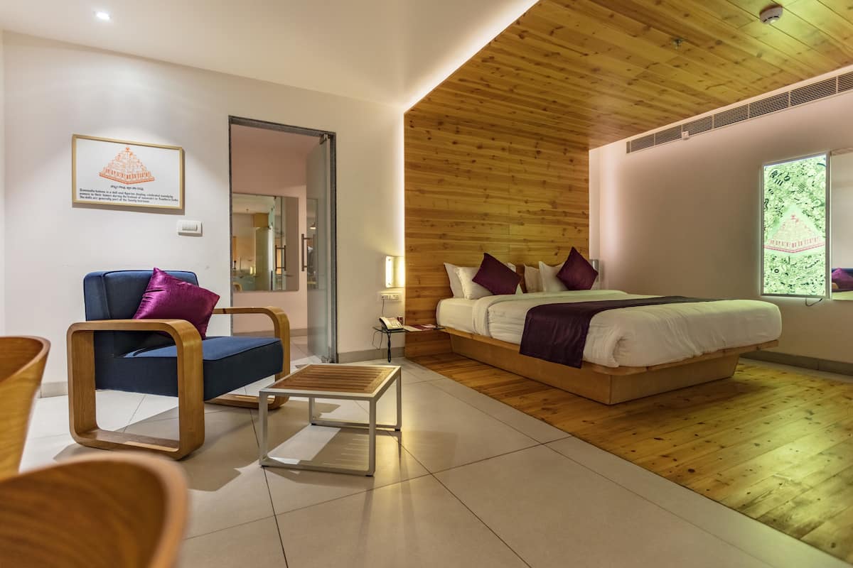 Ein modernes Schlafzimmer mit Holzboden, einem Bett mit weißer Bettwäsche und violetten Kissen, einem blauen Sofa mit einem violetten Kissen und einem kleinen Holztisch.