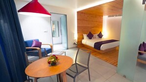 Une chambre d’hôtel moderne avec un mur d’accent en bois, un lit avec une literie blanche et violette, un luminaire suspendu rouge, une petite table ronde agrémentée d’un arrangement floral et un ventilateur de plafond.