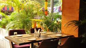 Un coin repas avec une table dressée pour deux, entouré d’une végétation luxuriante et offrant une vue sur un marché aux couleurs vives.