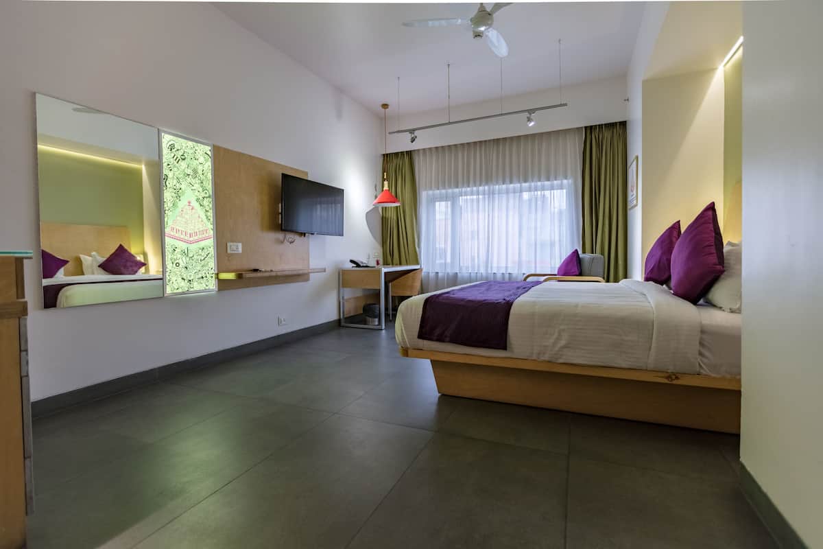 Ein modernes Hotelzimmer mit einem großen Bett, einem Schreibtisch, einem Flachbildfernseher und einem großen Spiegel.