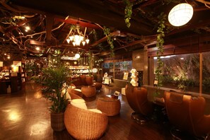 A cozy lounge area with wicker furniture, a bar in the background, and a large window with a view of a rocky landscape. - Hotel Bali An Resort Shinjuku Island - Adults only (Tokyo)