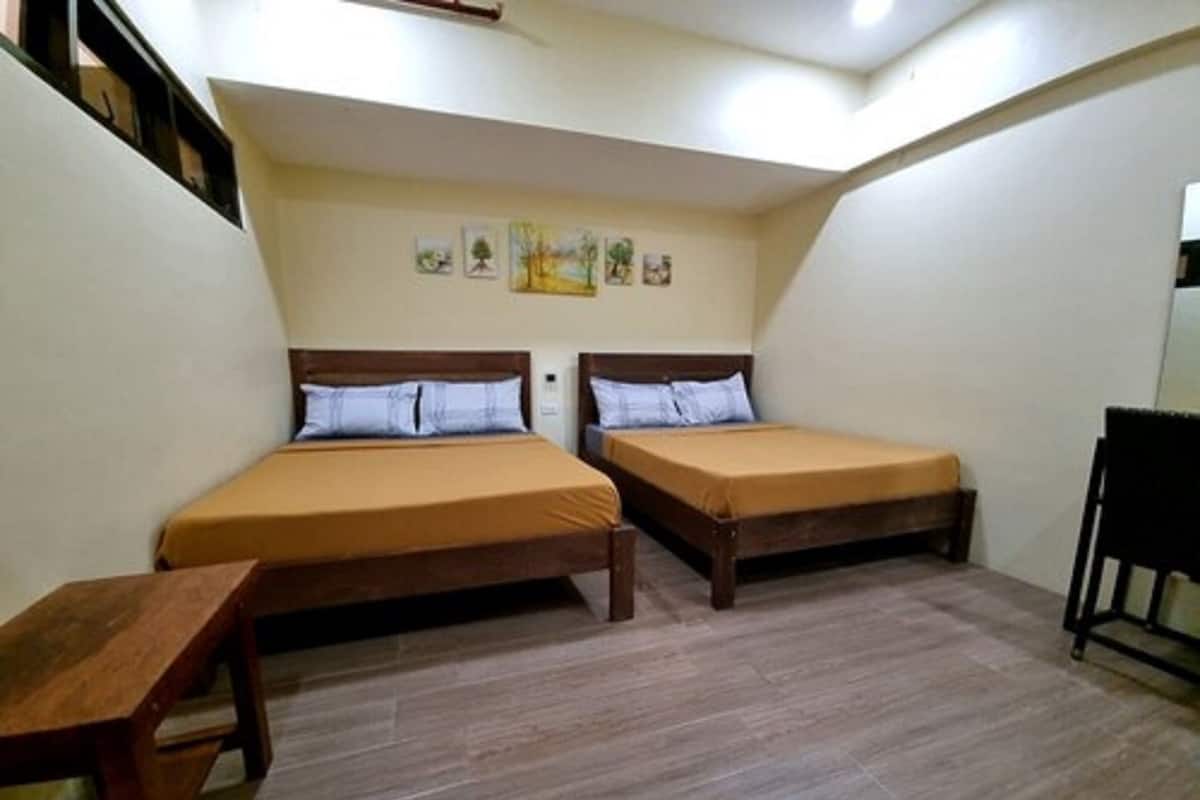 A small, compact room with two single beds, a wooden table, and a chair.