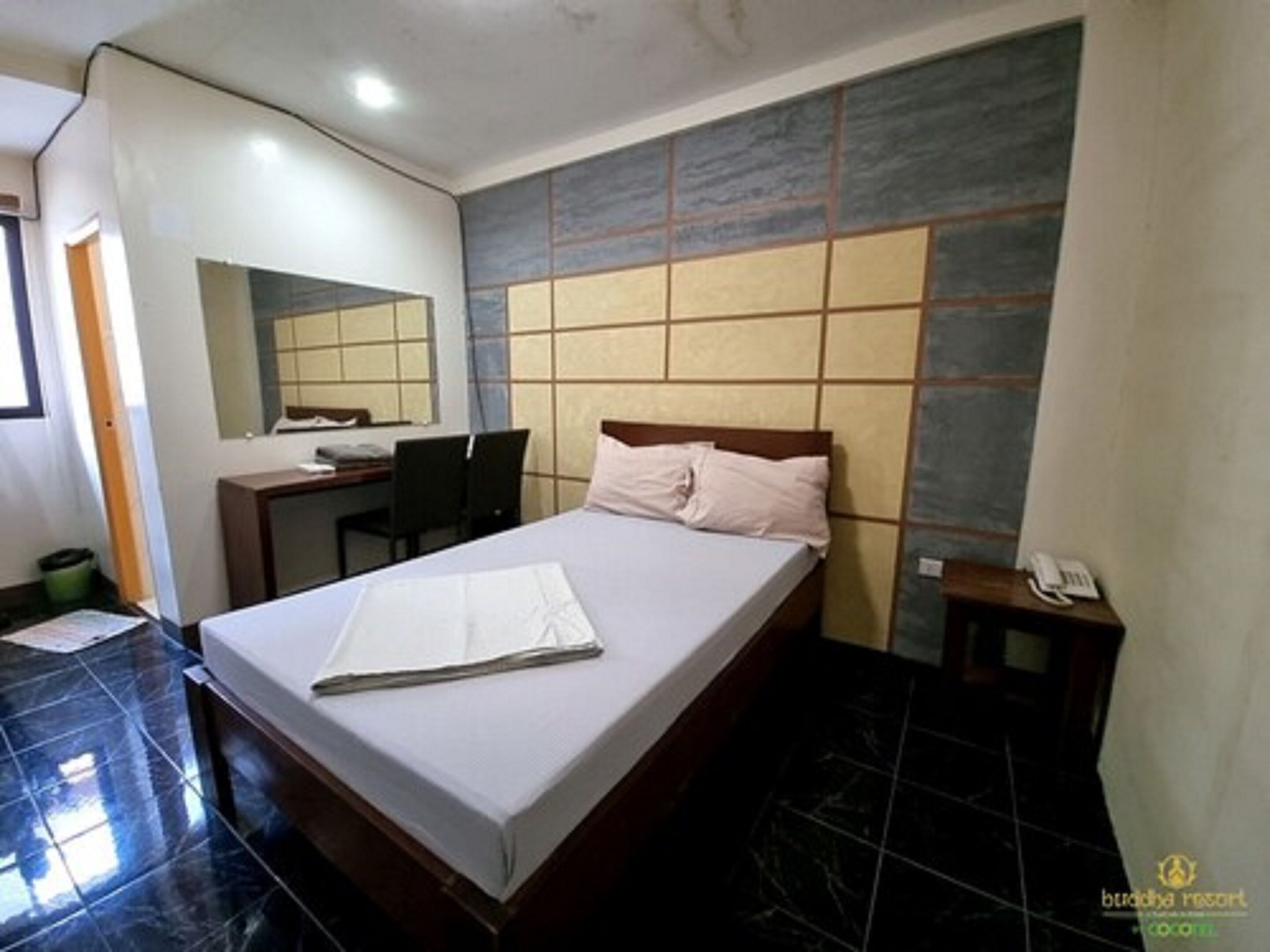 Una habitación de hotel con una cama, un escritorio, una silla, un espejo y un teléfono sobre una mesita de noche.