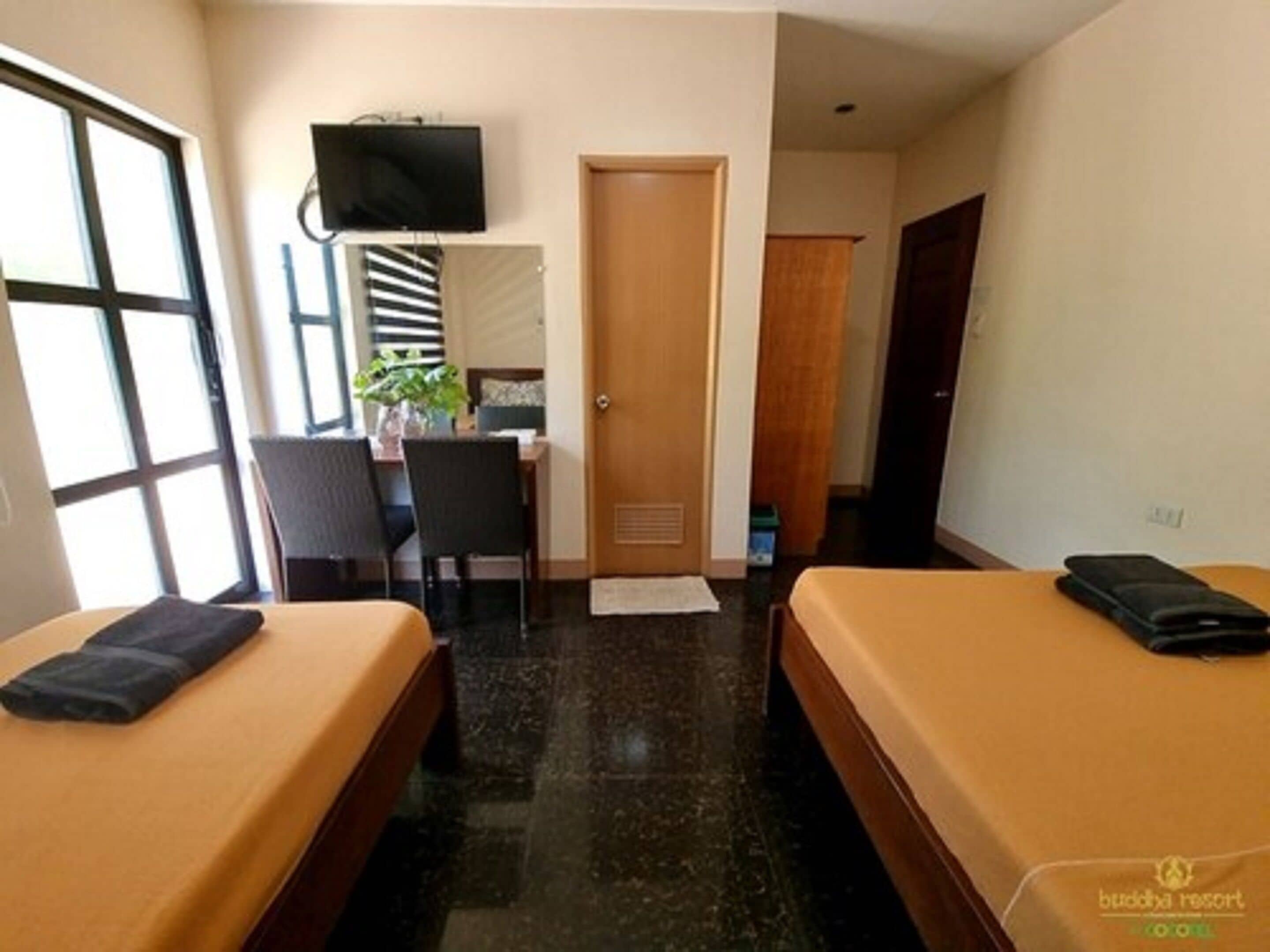 A hotel room with two beds, a desk, a chair, a television, and a door.