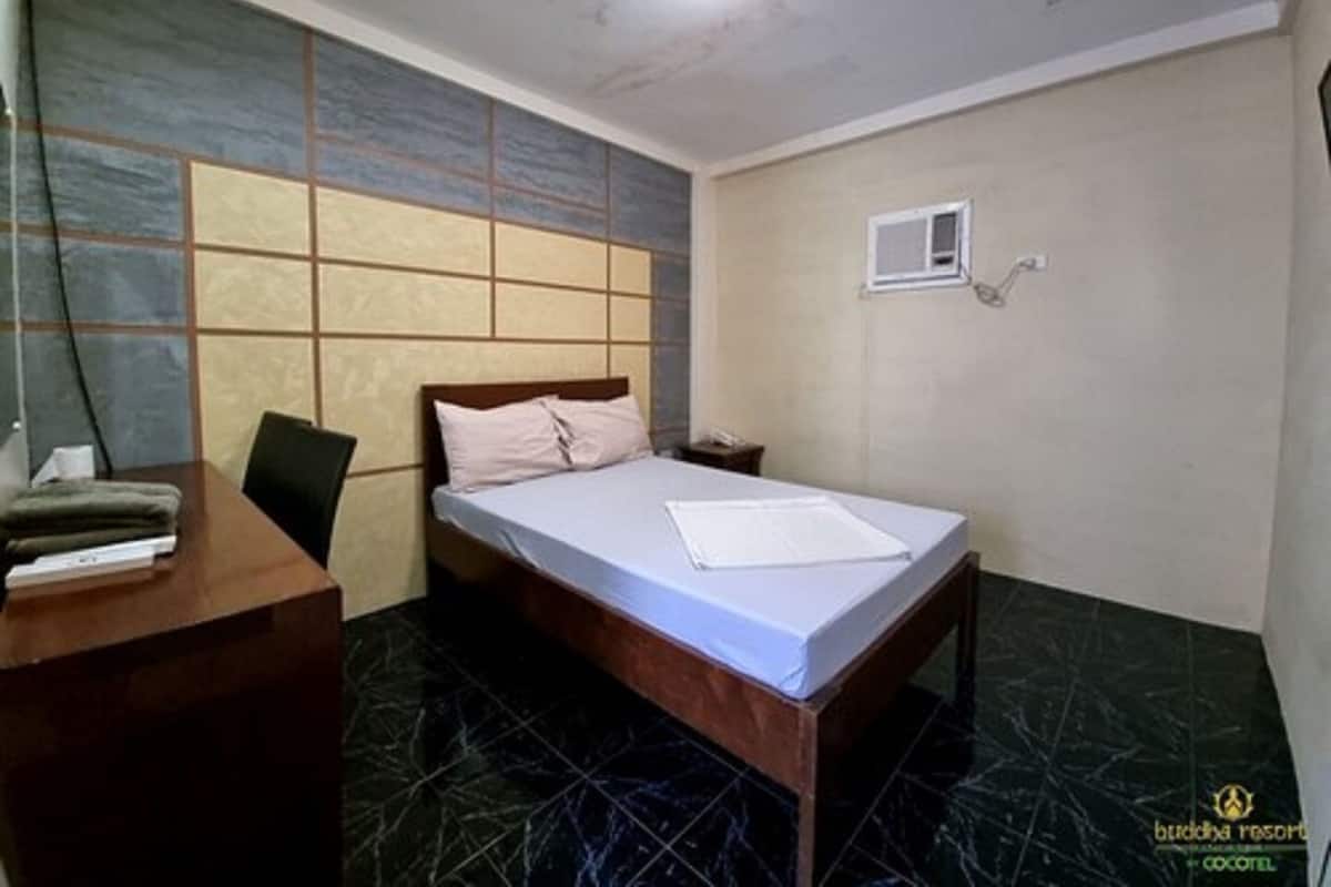 A hotel room with a bed, a desk, and a chair. There is a small window on the wall.